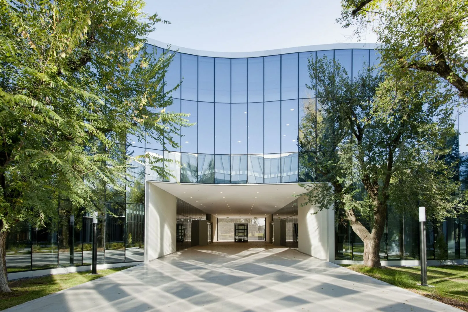 The curved glass façade and covered entrance of Pabellón Cero + Infinito, surrounded by trees